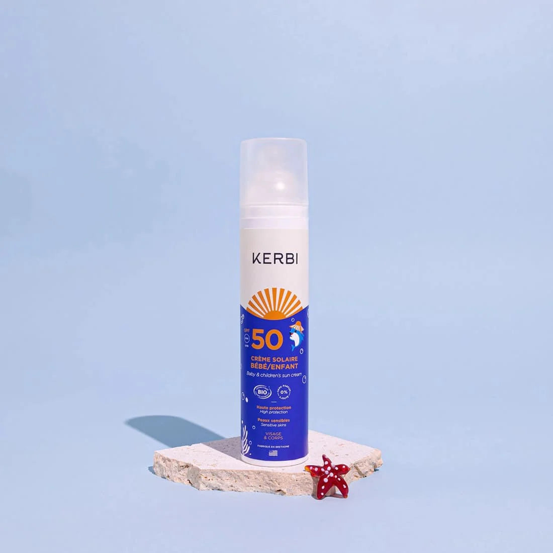 Kerbi Aurinkovoide Lapsille SPF 50; valkoinen pullo tekstillä ”KERBI SPF 50” pystyssä suorakaiteen muotoisella kivilaatalla; pullo mattapintainen pyöristetyin reunoin, lihavoitua groteskikirjasinta tuotenimelle; laatan edessä pieni punainen meritähti sekä pullon etiketissä näkyvää aurinkosuojatietoa; tausta yksivärinen sininen; ei ihmisiä tai käsiä tuotekuvassa.