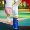 Kerbi Aurinkovoide Lapsille SPF 50; valkoinen muovipullo tekstillä ”Kerbi SPF 50 sunscreen for babies and children” pystyssä monivärisellä alustalla ulkona; pullo kiiltäväpintainen yksinkertaisella, lihavoidulla typografialla etiketissä; sumeana taustalla leikkivä lapsi vaaleanpunaisessa hameessa.