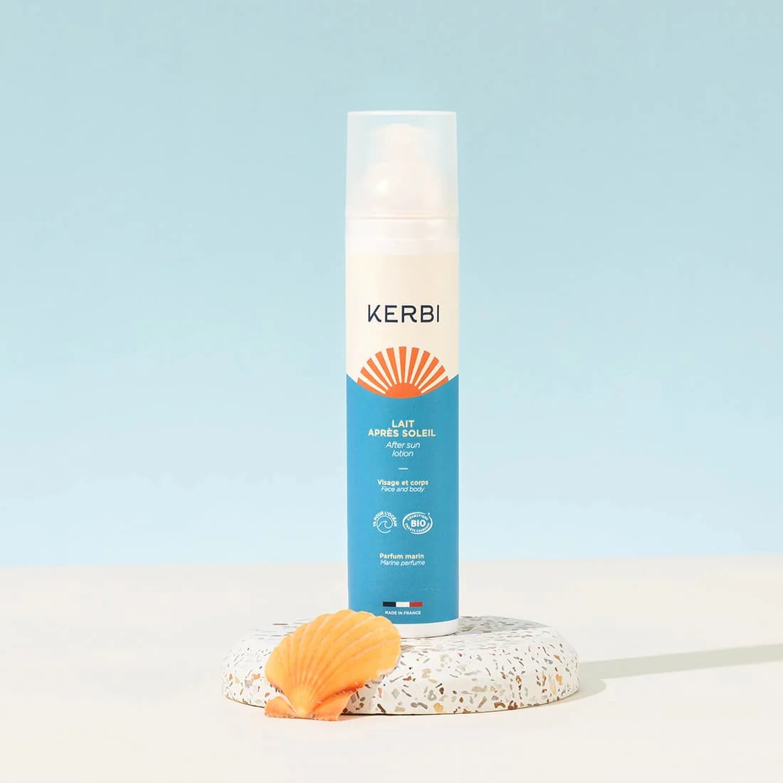 Kerbi After Sun Voide; sininen ja valkoinen pullo tekstillä ”KERBI” pystyssä terratsokorokkeella, vieressä oranssi simpukankuori, vaaleansinistä taustaa vasten; pullo lieriömäinen mattapinnalla, etiketissä yksinkertaista groteskikirjasinta; ei ihmisiä tai käsiä kuvassa; kuva otettu edestä silmien tasolta.