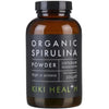 Kiki Health Luomu Spirulina-jauhe; ruskea sylinterinmuotoinen pullo mustalla kierrekorkilla, mattapintainen viimeistely ja suorakulmainen etiketti etupuolella; etiketissä valkoista ja vihreää groteskitekstiä mustaa taustaa vasten; luettavassa tekstissä lukee ruskea pullo, merkitty Organic Spirulina Powder, 100-prosenttisesti raakoja ainesosia, runsaasti proteiinia ja antioksidantteja, 200 g, KIKI Health; valkoinen tausta, studiotuotekuva, ei ihmisiä tai käsiä näkyvissä.