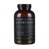 Kiki Health Natures Living Luomu Superfood-jauhe; ruskea pullo, merkitty Natures Living Superfood by Kiki Health, sisältää 150 g jauhemaista lisäravinnetta vihreistä kasveista, kasvimehuista, merikasveista, entsyymeistä ja hyödyllisistä bakteerikannoista; pullo on sylinterinmuotoinen kiiltäväpinnalla mustalla kierrekorkilla; etiketissä groteskitekstiä valkoisena ja vihreänä mattamustalla pohjalla; tuote kuvattu valkoista taustaa vasten, ei ihmisiä tai käsiä näkyvissä.