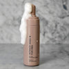 LIP Intiimipesuaine Miehille; beige pullo, jossa lukee "Intimate Wash for Men", seisoo marmoripinnalla, valkoista vaahtoa valuu mattapintaisesta annostelijasta yli; etiketin teksti on yksinkertaista, mustaa ja groteskia; suorakulmaisessa pullossa on pyöristetyt reunat eikä näkyviä kuvioita; tausta on harmaa ja marmoroitu läpi kuvan, kuvassa ei ihmisiä tai käsiä.