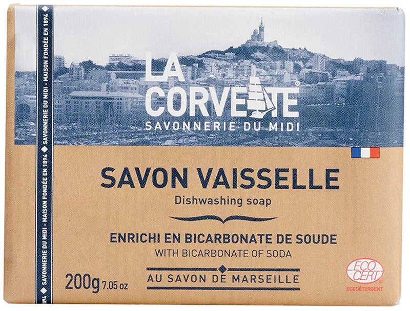 La Corvette Astianpesusaippua; La Corvette-astianpesusaippuapala, 200 g, esillä Marseillen kaupunkimaiseman edessä; pakkaus suorakaiteen muotoinen mattaruskeaa paperia sinisin tehostein; ranskan- ja englanninkielistä tekstiä lihavoidulla groteskikirjasimella, näkyvissä ECOCERT-logo; ei ihmisiä tai käsiä kuvassa; tuote keskitettynä suorassa kuvassa.