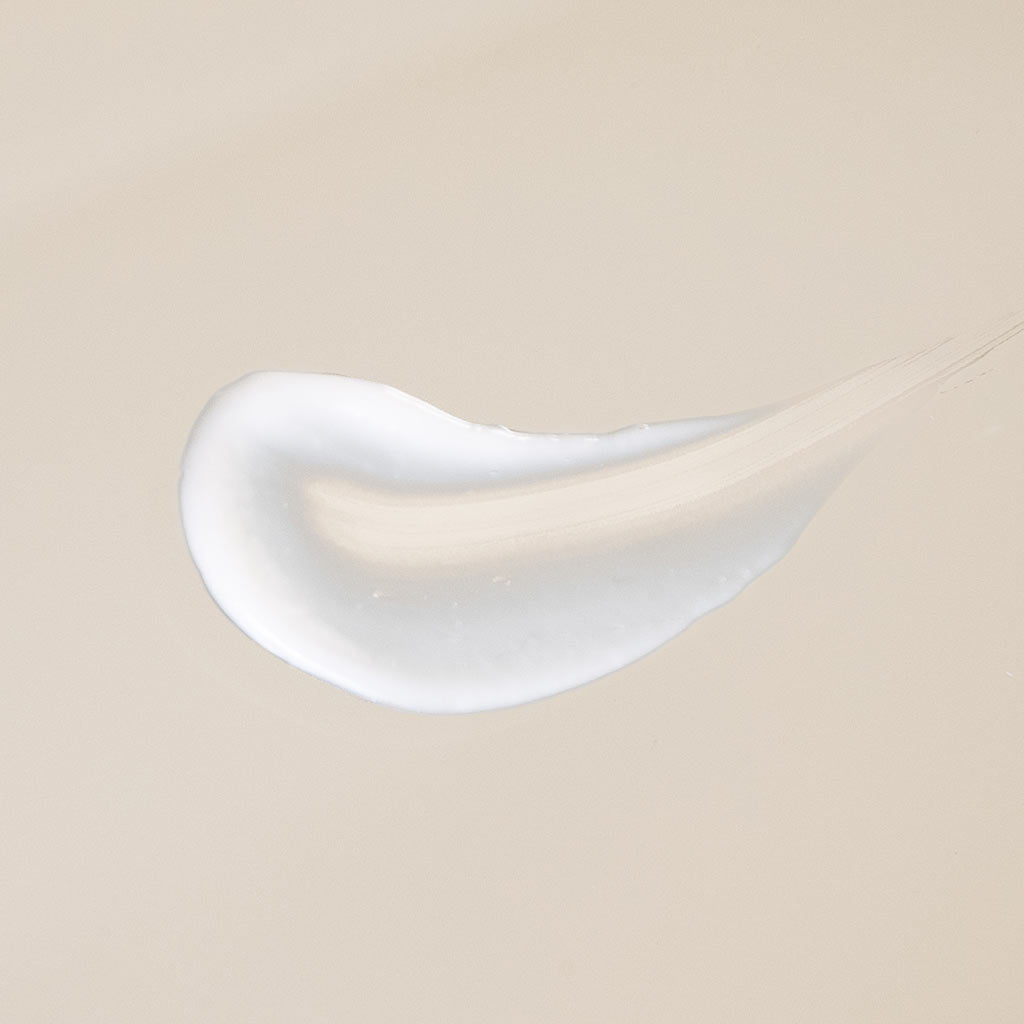 Laboratoires de Biarritz Anti Dark Spot Night Cream: lähikuva sileästä, valkoisesta voiteesta, joka on levitetty beigelle pinnalle kaarevaksi pisaramaiseksi läiskäksi kiiltävällä, kosteuttavalla tekstuurilla; pakkausta, tekstiä tai logoja ei näy kuvassa; tausta täyttää koko kuva-alan, ei ihmisiä tai käsiä näkyvissä.
