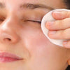 Laboratoires de Biarritz Cleansing Care Biphase Make-up Remover Eyes & Lips; henkilö pyyhkii varovasti suljettua silmäänsä pehmeällä puuvillatyynyllä, keskittyen rauhoittavaan ihonhoitoon tai hienovaraiseen meikinpoistoon; puuvillatyyny pyöreä ja valkoinen tekstuurisella mattapinnalla; kättä pitävä käsi puhdas, kynnet luonnolliset; ei tuotepakkausta tai brändäystä näkyvissä; tausta tasainen, epätarkka ja neutraalinvärinen; lähikuva korostaa silmäaluetta ja puuvillatyynyn kosketusta.