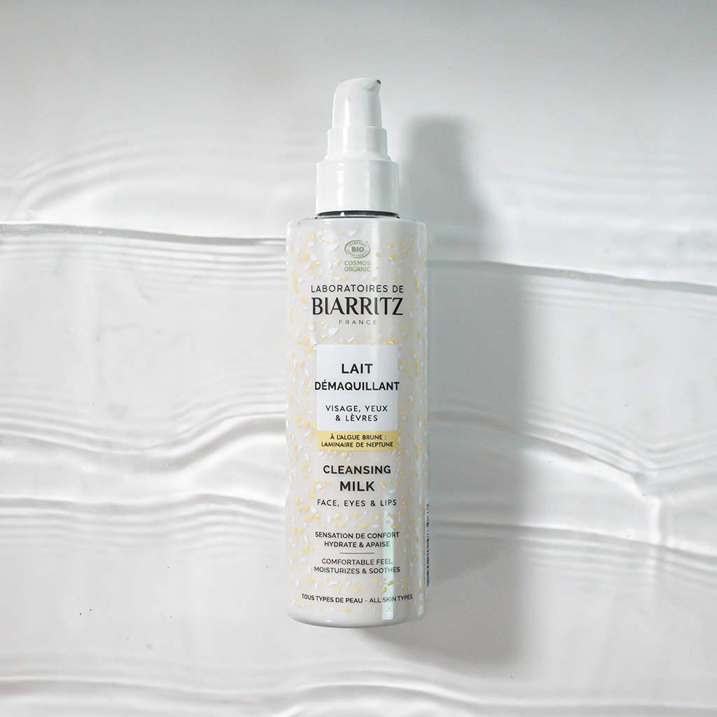 Laboratoires de Biarritz Cleansing Care Puhdistusmaito; valkoinen pumppupullo Biarritz-puhdistusmaidolle valkoisella tekstuuripintaisella alustalla; lieriön muotoinen muovipullo mattapinnalla; etiketissä ranskan- ja englanninkielinen teksti groteskifontilla, mainitaan sopivuus kasvoille, silmille ja huulille; ei ihmisiä tai käsiä; kuvattu ylhäältä kulmassa.
