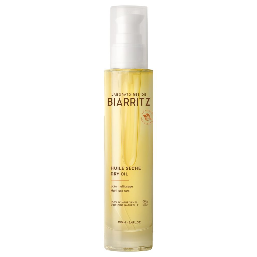 Laboratoires de Biarritz Dry Oil Kuivaöljy; kirkas sylinterin muotoinen pullo Laboratoires de Biarritz Huile Sèche Dry Oil -kuivaöljyä valkoisella muovipumpulla ja sileällä kiiltopinnalla, sisältää keltaista öljyä; etuetiketti kaksikielinen ranska-englanti groteskikirjasimella, näyttää brändinimen, tuotenimen ja tilavuuden 100 ml (3,4 fl. oz); tausta tasainen ja pelkistetty, ei ihmisiä tai käsiä.