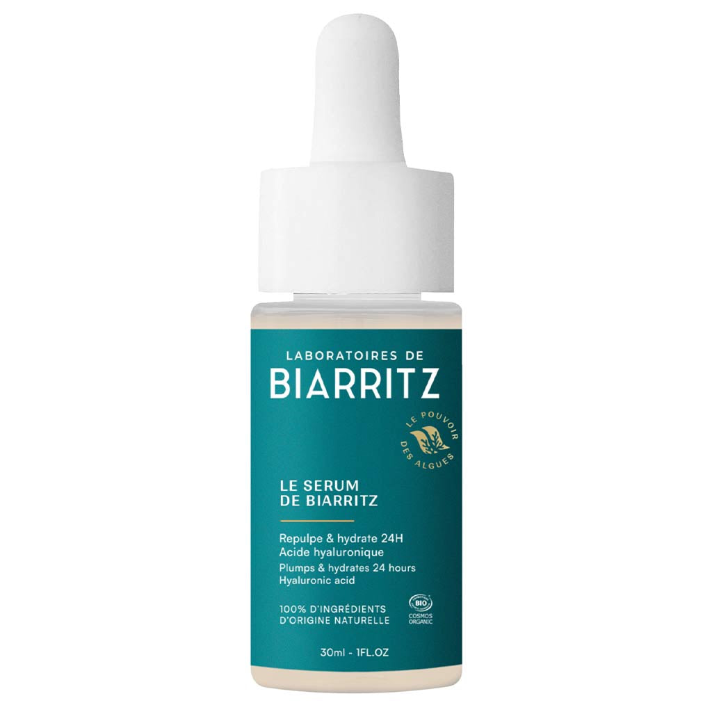 Laboratoires de Biarritz Le Sérum de Biarritz Face Serum: turkoosi-valkoinen tiputinpullo lasista, mattapintainen etiketti groteskikirjasimella, sylinterimäinen muoto, 30 ml:n koko; tekstissä mainitaan hyaluronihappo ja 24 tunnin kosteutus; tausta on neutraali, tuote keskellä kuvaa, ei ihmisiä tai muita esineitä näkyvissä.