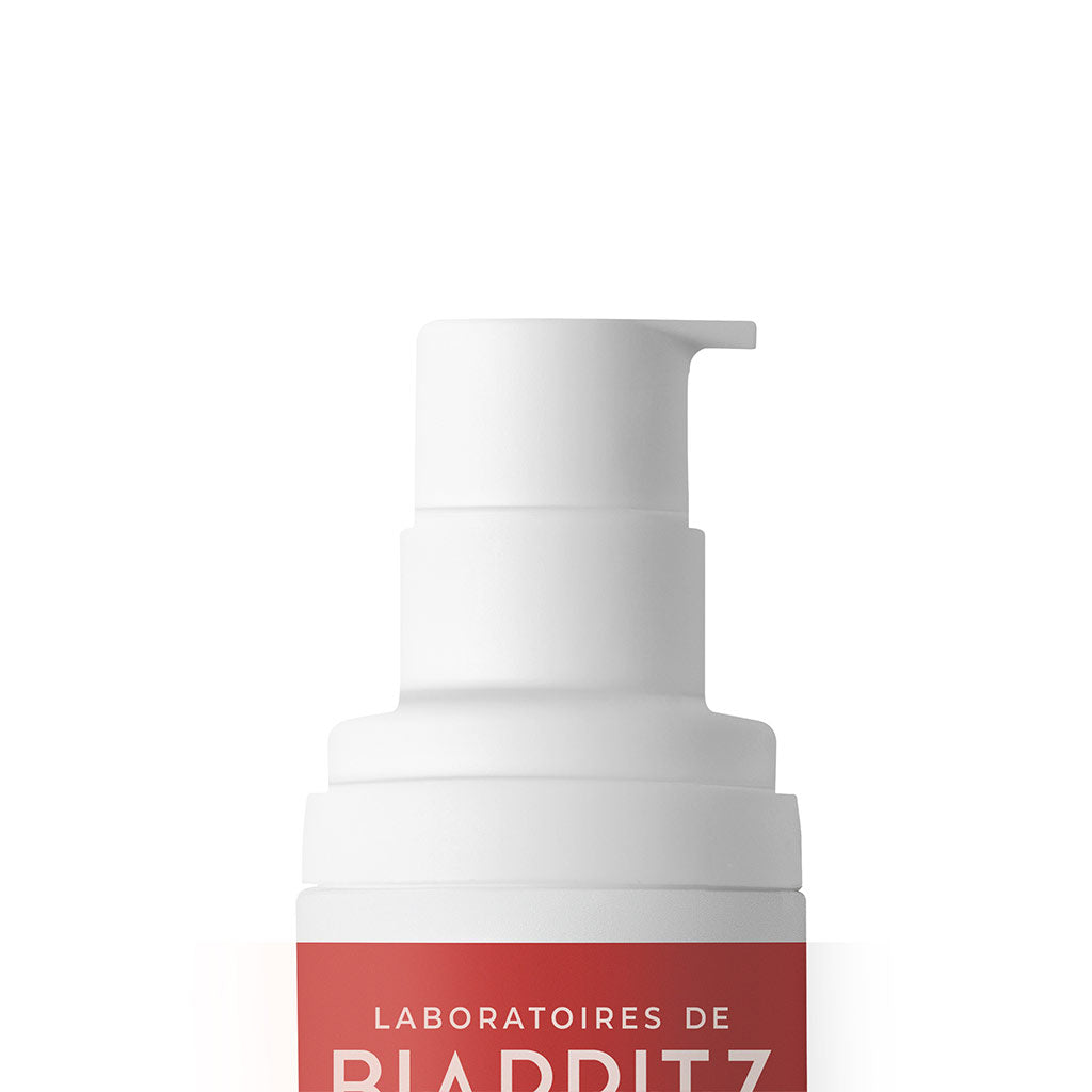 Laboratoires de Biarritz Suncare Invisible Lotion SPF50; valkoinen muovinen pumppupullo punaisella etiketillä, osittainen teksti lukee LABORATOIRES DE BIA... valkoista taustaa vasten; pullo sylinterin muotoinen sileällä kiiltopinnalla; etiketissä suuraakkosin groteskikirjasin valkoisena; ei ihmisiä tai käsiä kuvassa; tuote keskitettynä yksinkertaiseen studiokuvaan tasaisessa valaistuksessa.