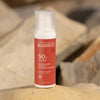Laboratoires de Biarritz Suncare Invisible Lotion SPF50; valkoinen sylinterin muotoinen pullo Laboratoires de Biarritz SPF 50 -näkymätöntä aurinkovoidetta mattapinnalla seisoo pystyssä tasaisella beigellä kivellä; korkki myös valkoinen ja vaikuttaa muovilta; etikettiteksti näyttää brändinimen ja SPF-tiedot yksinkertaisella groteskikirjasimella; sumeana taustalla tekstuurisia kiviä sinivihrein mineraalikerrostumin; ei ihmisiä tai käsiä.