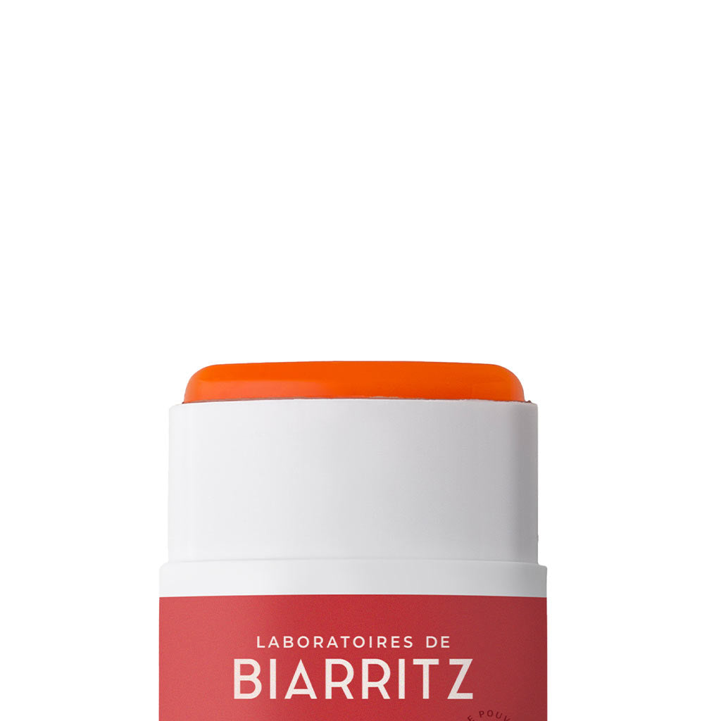 Laboratoires de Biarritz Suncare Invisible Sun Stick SPF50+; lähikuva puikkopakkauksesta tekstillä Laboratoires de Biarritz, näyttää oranssia balsamia esillä yläosassa valkoista taustaa vasten; sylinterin muotoinen pakkaus valkoista muovia mattapinnalla ja pyöristetyin reunoin; mustaa groteskityypografiaa näyttää brändinimen ja tuotetiedot; ei ihmisiä tai käsiä kuvassa.