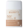 Laboratoires de Biarritz Tinted Sunscreen Stick SPF50+ (Sävytetty Aurinkovoidepuikko): valkoinen ja beige sylinterimäinen puikko mattapinnalla, lihavoitu groteskiteksti; etiketissä maininnat epäpuhtauksien ja arpien peittämisestä, luomusertifikaattien logot sekä sävytetty suoja; muovinen pakkaus, tuotetiedot painettu suoraan etikettiin; tausta on valkoinen, tuote keskellä kuvaa, ei ihmisiä tai käsiä näkyvissä.