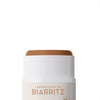 Laboratoires de Biarritz Tinted Sunscreen Stick SPF50+: lähikuva valkoisesta sylinterimäisestä puikkopakkauksesta, jonka yläosasta pursuaa ruskeansävyistä tuotetta; etiketissä musta-ruskea groteskiteksti tuotenimelle; pinta on mattaa ilman muita merkintöjä; tausta on valkoinen, ei ihmisiä tai käsiä kuvassa.