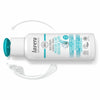 Valkoinen Lavera Moisture & Care -hoitoainepullo turkoosilla korkilla makaa kyljellään, vieressä hieman läikkynyttä hoitoainetta; etiketissä vegaanituotetiedot englanniksi ja italiaksi sinisellä ja mustalla tekstillä; pullo on lieriömäinen kiiltäväpintainen, groteskikirjasin painettuna etikettiin; tausta yksinkertainen, ei ihmisiä tai muita esineitä; kamerakulma näyttää tuotteen kokonaan sivulta läheltä kuvattuna.
