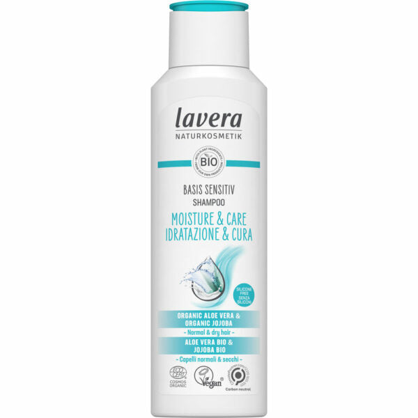 Valkoinen Lavera Basis Sensitiv Shampoo -pullo normaalille ja kuivalle hiukselle, sinisin yksityiskohdin ja tekstillä kosteudesta ja hoidosta, sisältää luomualoeveraa ja jojobaöljyä; pakkauksessa vegaani- ja luonnonkosmetiikkasertifikaattien logot, korostaen hellävaraista kosteutusta luonnollisilla raaka-aineilla; pullo pystyasennossa, muovia kiiltäväpinnalla, pyöristetyt reunat, kirkas korkki, groteskikirjasin etiketissä; tausta yksinkertainen, ei ihmisiä näkyvissä.