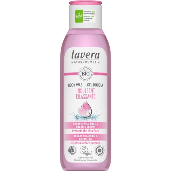 A pink plastic bottle of Lavera Naturkosmetik Body Wash with a matte finish, slim cylindrical shape, and flip-top cap. Front label shows “Indulgent Rilassante,” “organic wild rose and cotton,” vegan and climate-neutral claims, and floral graphics. Branding uses bold sans-serif text. No people or hands are present. Neutral background with standard product shot framing.