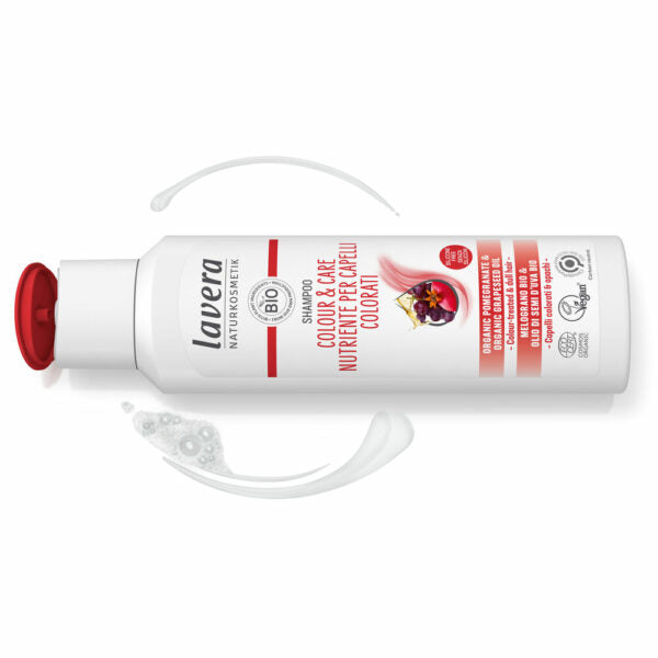 Valkoinen muovipullo Lavera Color & Care Shampoo -tuotetta punaisella läppäkorkilla, kuvattu pystyasennossa; pullon pinta mattainen, muoto hieman kaareva suorakaide; etusivun etiketissä granaattiomena- ja quinoakuvitus sekä selkeä groteskiteksti tuotenimelle; pullon vierellä valkoisia vaahtopyörteitä vaalealla, tasaisella taustalla.