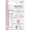 Lavera Sheer Lip Balm -huulivoidepakkaus valkoisessa ja vaaleanpunaisessa muotoilussa, jossa korostetaan luomuraaka-aineita, vegaanisertifikaattia ja kierrätysmateriaalin käyttöä; lieriömäinen mattapintainen huulivoideputkilo esitetään litteän suorakaiteen muotoisen pahvitaustan vieressä; etiketissä groteskikirjasin, osa tekstistä lihavoitua; ei ihmisiä näkyvissä, tausta yksinkertainen, tuotekuva edestä.
