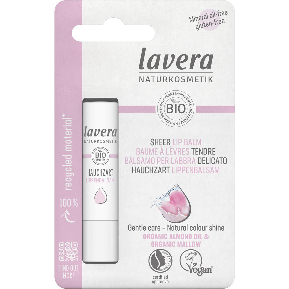 Lavera Sheer Lip Balm -huulivoidepakkaus valkoisessa ja vaaleanpunaisessa muotoilussa, jossa korostetaan luomuraaka-aineita, vegaanisertifikaattia ja kierrätysmateriaalin käyttöä; lieriömäinen mattapintainen huulivoideputkilo esitetään litteän suorakaiteen muotoisen pahvitaustan vieressä; etiketissä groteskikirjasin, osa tekstistä lihavoitua; ei ihmisiä näkyvissä, tausta yksinkertainen, tuotekuva edestä.