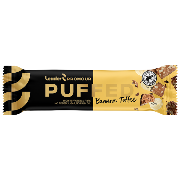 Leader Promour Puffed Banana Toffee -patukan keltainen ja musta kääre, jossa kuvia patukasta ja sen raaka-aineista; mattapintainen pakkaus serifi- ja groteskikirjasimin; etusivulla tuotenimi, maku sekä kuvakkeet tai teksti runsaasta proteiinista, kuidusta, ilman lisättyä sokeria ja ilman palmuöljyä; patukan muoto suorakaiteen mallinen; neutraali studiotausta ilman käsiä tai ihmisiä.