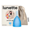 Lunette Kuukautiskuppi Sininen, sininen kuppi Lunette-rasian ja harmaan vetonyörillisen pussin edessä, rasiassa kukkakuvitus