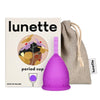 Lunette Kuukuppi Violetti, violetti mattapintainen kuukuppi pystyssä pakkauksen edessä (naisen kuvitus), vieressä beige narupussi sinisellä "Lunette"-tekstillä