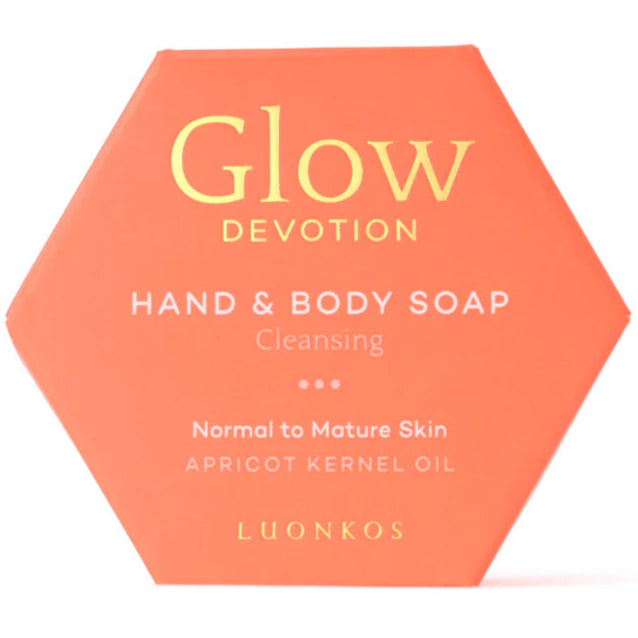 Luonkos Glow Devotion Hand & Body Soap; kuusikulmainen oranssi rasia mattapinnalla, tekstillä ”Glow Devotion Hand & Body Soap Cleansing”, rikastettu ravitsevalla aprikoosinsiemenöljyllä normaalille ja kypsälle iholle, valmistaja Luonkos; rasia pahvia, lihavoitua mustaa tikkukirjasinta; tuote kuvattu tasaisella valkoisella taustalla ilman ihmisiä tai rekvisiittaa.