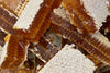 Close-up of stacked honeycomb pieces with golden raw honey visible inside the hexagonal cells and a white waxy surface on top. Product: natural honeycomb. Color: golden yellow (honey), white (waxy tops). Material: beeswax, raw honey. Surface finish: glossy in cells, matte on waxy sections. Shape: irregular rectangles, hexagonal cell structure. No packaging, labels, or text present. Neutral background.
