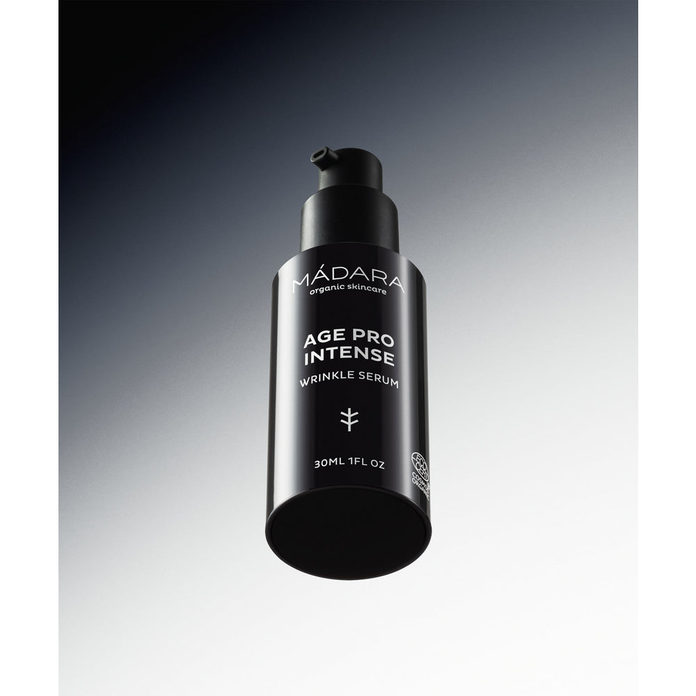 Madara AGE PRO Intense Wrinkle Serum; musta pullo Mádara Age Pro Intense Wrinkle Serum -tuotetta, 30 ml, pumppuannostelijalla keskellä kuvaa; pullon pinta on mattapintainen ja sylinterinmuotoinen, etiketissä valkoista groteskitekstiä sisältäen tuotenimen ja tilavuuden; tausta on harmaa liukuväri; ei ihmisiä tai käsiä kuvassa.