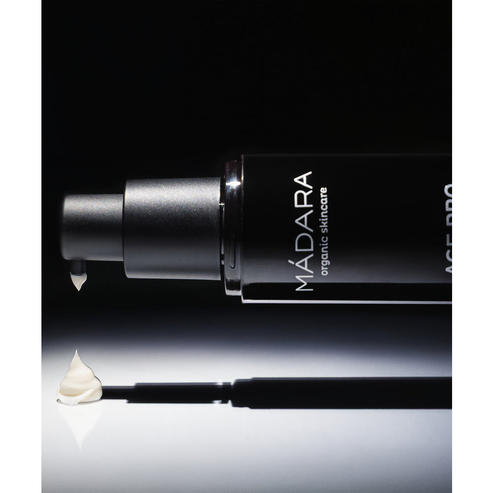 Madara AGE PRO Renew Night Cream; musta sylinterinmuotoinen muovipullo Mádara-luonnonihonhoitovoidetta on aseteltu vaakasuoraan sileälle, valkoiselle taustalle; pullon pinta on mattapintainen ja siinä on pieni, suuraakkosin valkoinen groteskimerkintä; pieni määrä voidetta on annosteltu pyörteenä pullon suuaukon vieressä; ei ihmisiä näkyvissä; voimakas valaistus luo selkeitä varjoja kohtaukseen.