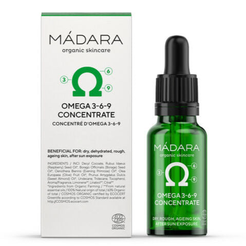 Madara Omega 3-6-9 Concentrate; vihreä lasinen tiputinpullo ja sen laatikko, merkitty Mádara Organic Skincare Omega 3-6-9 Concentrate, tarkoitettu kuivalle, kuivuneelle tai ikääntyneelle iholle, tuo tärkeitä omega-rasvahappoja ihon ravitsemiseen ja elvyttämiseen; molemmat esineet mattapintaisia; pullo on sylinterinmuotoinen valkoisella tiputinkorkilla; laatikossa minimalistista typografiaa valkoisella tummaa taustaa vasten; ei ihmisiä tai käsiä näkyvissä; tausta vaalea ja hyvin valaistu.