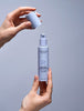 Madara Retinol Alternative Plant-Powered Day Cream; kaksi kättä pitelee MÁDARA Retinol Alternative -voidepulloa; toinen käsi poistaa korkin, toinen pitelee vegaanista koostumusta sisältävää pulloa vaaleaa taustaa vasten; tuote on sylinterinmuotoisessa astiassa mattavalkoisella pinnalla, mustalla pumpulla ja mustalla groteskitekstillä etiketissä; vain ”MÁDARA Retinol Alternative” on selvästi luettavissa; kuvassa pehmeä, tasainen valaistus eikä muita esineitä.