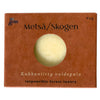 A brown matte-finish rectangular box labeled Metsä/Skogen features a circular transparent window showing a round, solid cream-colored item inside. The box has legible text: Kukkaniitty voidepala, responsible forest-luxury, and 60g in simple sans-serif font. No people or hands are visible. Neutral background with minimal context shown.