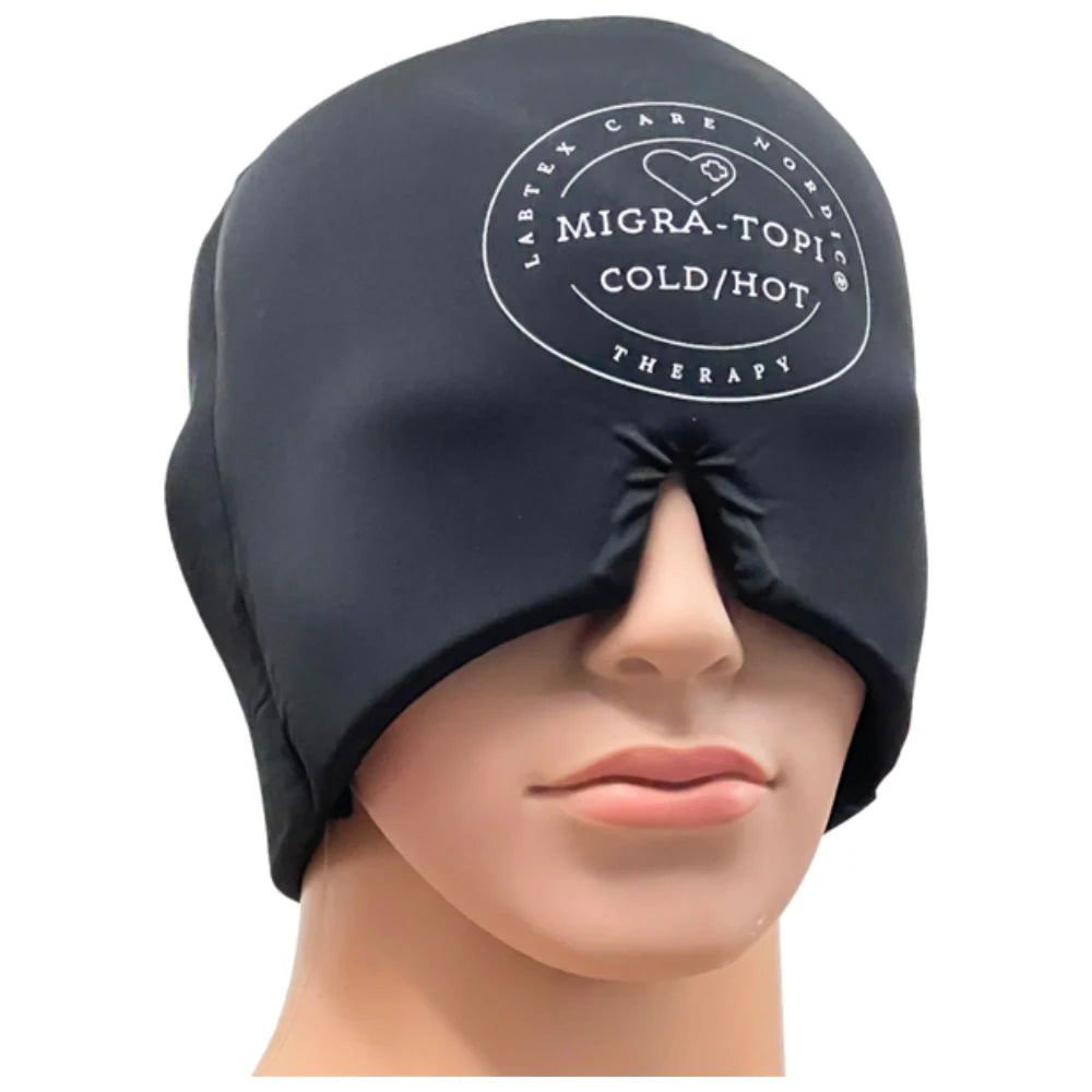 A mannequin head displays a black cold/hot therapy cap with a soft, matte finish that covers the forehead, eyes, and crown. The cap features white Migra-Topia text logo on the front in clean sans-serif lettering. No packaging is visible. The background is plain and evenly lit, with no people or actions shown. A mannequin head wears a black Migra-Topia cold/hot therapy cap that covers the forehead, eyes, and top of the head, featuring the product logo on the front for effective migraine relief.