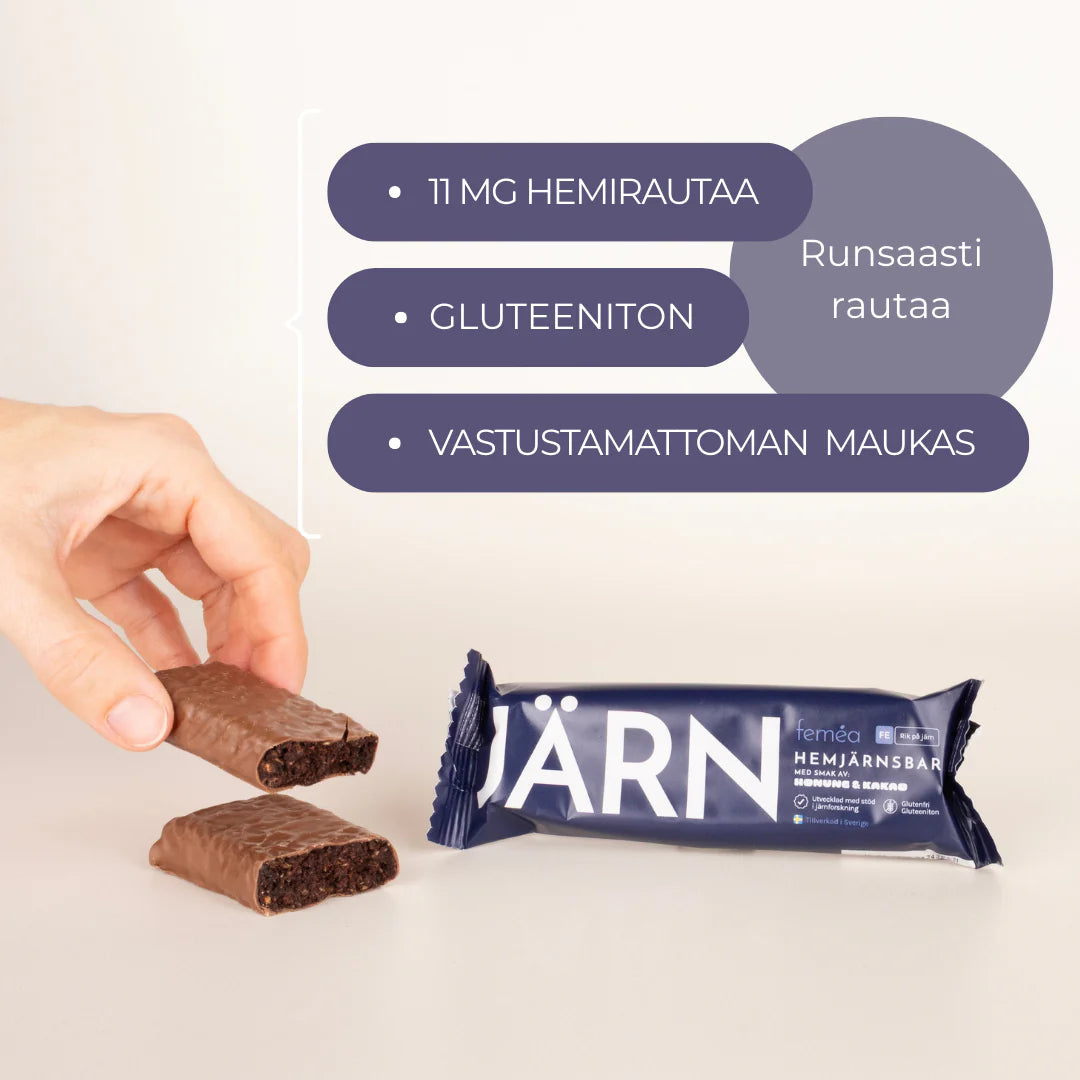Mini Ferrum Feméa Hemirautapatukka; käsi pitelee halkaistua suklaapatukkaa suorakulmaisen JÄRN-kääreisen patukan yläpuolella mattapinnalla; kääre pääosin vaalea, lihavoitua groteskikirjasinta mustana ja punaisena; luettavassa etiketissä: 11 mg hemirautaa, gluteeniton, houkuttelevan maukas, runsaasti rautaa (suomeksi); tausta neutraali ja pelkistetty.