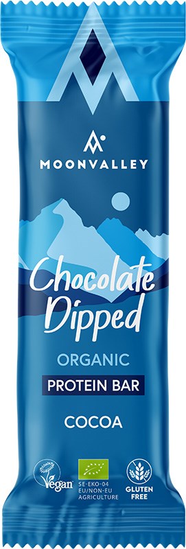 Moonvalley Luomu Proteiinipatukka Kaakao; sininen Moonvalley Chocolate Dipped Organic Protein Bar -kääre, kaakao-maku; suorakulmainen matta muovipakkaus valkoisella ja kultaisella tekstillä näyttää tuotenimen ja maun; etupuolella vegaani-, EU-luomu- ja gluteenittomuuskuvakkeet sekä tyylitelty valkoinen vuorigrafiikka taustalla; ei ihmisiä tai muita esineitä, tasainen tausta, lähikuva.