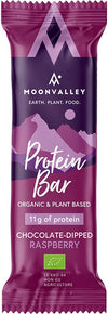 Moonvalley Luomu Proteiinipatukka Vadelma; violetti Moonvalley-proteiinipatukan kääre tekstillä Earth. Plant. Food. ja vuorikuvituksella, luettavissa Organic & Plant Based, 11 g proteiinia ja Chocolate-Dipped Raspberry; suorakulmainen kääre mattapinnalla lihavoidulla valkoisella ja keltaisella groteskikirjasimella, tuotenimi ja ravintotiedot etupuolella; ei ihmisiä tai käsiä, tasainen tausta suoraan tuotekuvaan.