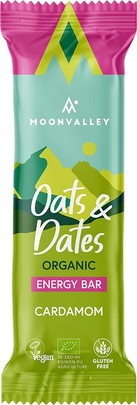 Moonvalley Luomu Energiapatukka Kardemumma; suorakulmainen energiapatukkapakkaus mattapinnalla tekstillä ”Moonvalley Oats & Dates Organic Energy Bar” kardemumma-maulla; hallitsevat värit vihreä ja vaaleanpunainen selkein vegaani- ja gluteenittomuusmerkein; tyylitellyt vuorigrafiikat taustalla; tuote kuvattu tasaista pintaa vasten, ei ihmisiä tai rekvisiittaa.