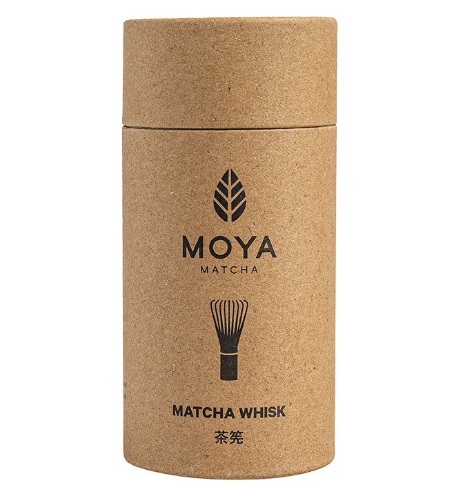Moya Matcha Matchavispilä; lieriömäinen mattapintainen pahvipurkki pystyssä vaalealla taustalla; pinnassa Moya Matcha -etiketti, yksinkertainen viivapiirros matchavispilästä, teksti Matcha Whisk ja sen alla japanilaisia merkkejä; groteskityypografia tasavälein; ei ihmisiä tai käsiä kuvassa.