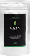 Moya Matcha Traditional Luomu Vihreä tee; hopeinen Moya Matcha Traditional -pakkaus mustalla etiketillä, eloisa vihreä lehtilogo ja teksti korostaa alkuperää arvostetulta Ujin alueelta Kioton prefektuurista Japanissa; pakkaus suorakaiteen muotoinen mattapinnalla; etiketin typografia moderni ja groteski; ei ihmisiä tai käsiä; valkoinen tausta, studiokuva.