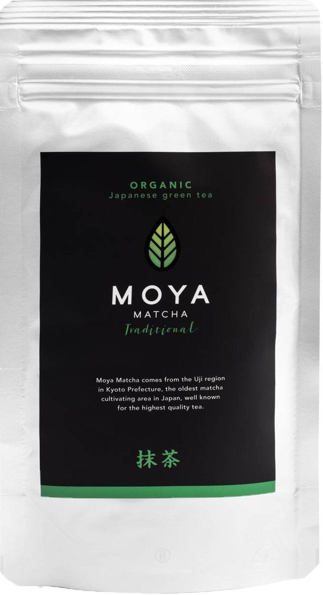 Moya Matcha Traditional Luomu Vihreä tee; hopeinen Moya Matcha Traditional -pakkaus mustalla etiketillä, eloisa vihreä lehtilogo ja teksti korostaa alkuperää arvostetulta Ujin alueelta Kioton prefektuurista Japanissa; pakkaus suorakaiteen muotoinen mattapinnalla; etiketin typografia moderni ja groteski; ei ihmisiä tai käsiä; valkoinen tausta, studiokuva.