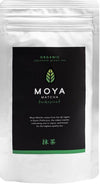 Moya Matcha Traditional Luomu Vihreä tee; hopeinen Moya Matcha Traditional -pakkaus mustalla etiketillä, eloisa vihreä lehtilogo ja teksti korostaa alkuperää arvostetulta Ujin alueelta Kioton prefektuurista Japanissa; pakkaus suorakaiteen muotoinen mattapinnalla; etiketin typografia moderni ja groteski; ei ihmisiä tai käsiä; valkoinen tausta, studiokuva.