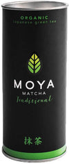 Moya Matcha Traditional Luomu Vihreä tee; korkea musta lieriömäinen metallipurkki mattapinnalla, etiketissä vihreä lehtilogo ja teksti kertoo luomulaatuisesta japanilaisesta seremoniamatchasta; purkissa istuva kansi; pakkauksessa valkoista groteskitekstiä; kuvattu edestä valkoisella taustalla, ei ihmisiä tai käsiä.