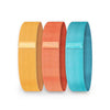Three fabric resistance bands in yellow, orange, and blue colors, each with a small rectangular label printed with “myoga” in lowercase sans-serif font. Bands have a matte finish and are cylindrical loops standing upright vertically in a straight line. No packaging or additional accessories are present. Background is plain white. No people or hands included.