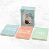 A box of Myga Yoga Pose Cards is displayed with three cards in front—Downward Facing Dog, Reclining Butterfly, and Tree—on a white marble surface. The box is rectangular, made of cardboard with a matte finish. Each card shows an illustrated yoga pose and pose name in clear sans-serif text. No people or hands are present. This is an overhead product shot against a smooth, patterned stone background.