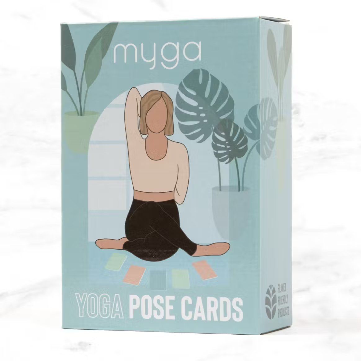A rectangular box with the label “myga YOGA POSE CARDS” shows an illustrated figure in a yoga pose, surrounded by tropical leaves and four small, colorful rectangular cards arranged below. Box design uses clear, bold sans-serif typography and has a matte finish. Text mentions “planet friendly product.” The item is photographed against a plain background in even lighting. A box labeled myga YOGA POSE CARDS features an illustration of a person in a yoga pose surrounded by tropical leaves and four colorful