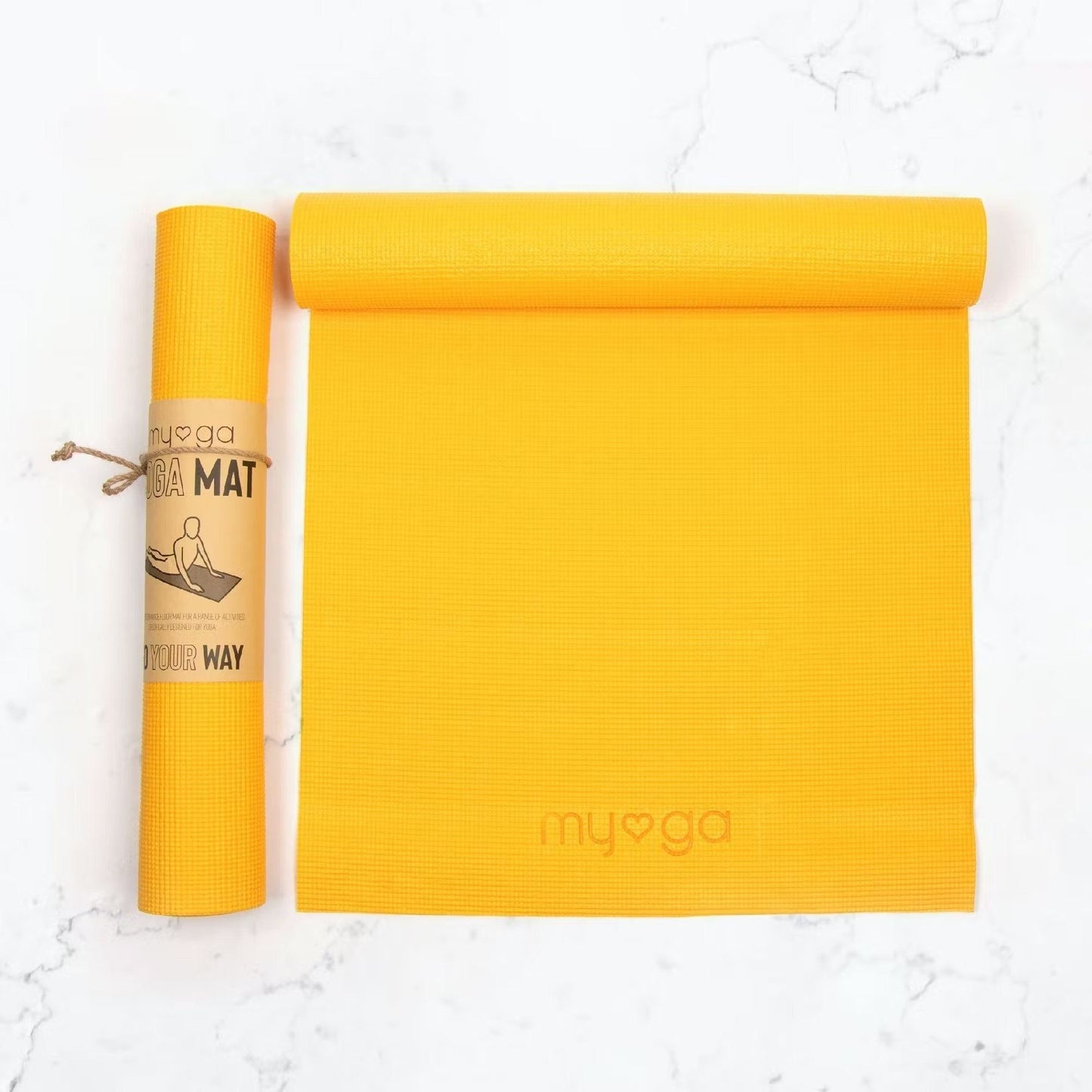 A bright yellow yoga mat is partially rolled out next to its rolled-up version, which features a brown paper label with printed yoga pose illustrations. Both mats are cylindrical in shape and have a matte finish. No typography is visible on the exterior of the mats or packaging. The products are positioned on a white marble surface with no people or hands present. The shot is directly overhead.