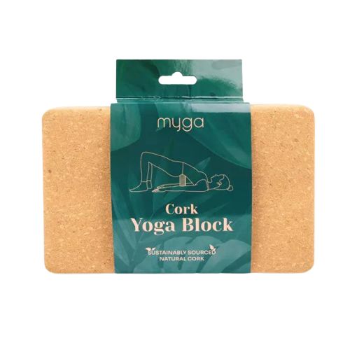 A rectangular cork yoga block with green paper packaging labeled Myga Cork Yoga Block, surface matte and light brown with visible cork texture. The label features a line drawing of a person in a bridge pose and sans-serif black text stating it is made from sustainably sourced natural cork and intended for eco-conscious yogis. Product is photographed against a plain white background.