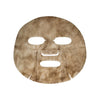 A flat, brown, coffee-infused face-shaped sheet mask with cutouts for the eyes, nose, and mouth, placed against a white background. The sheet material is matte and thin. There is no packaging or visible branding. No people or hands are in the shot. The image uses an overhead view to display the mask’s entire shape and surface clearly.