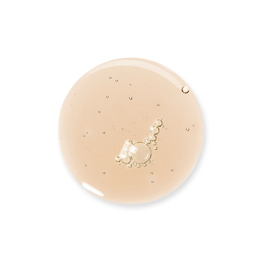 A close-up of a transparent, hydrating light beige liquid gel droplet with small air bubbles inside, isolated on a white background. Product type: liquid gel. Color: light beige. Material: gel consistency. Surface finish: glossy, reflective. Shape: irregular rounded droplet with visible smaller bubble shapes inside the main mass. No packaging or labels present in image. Background is solid white; no typography, people, or actions shown. Shot type is close-up detail.
